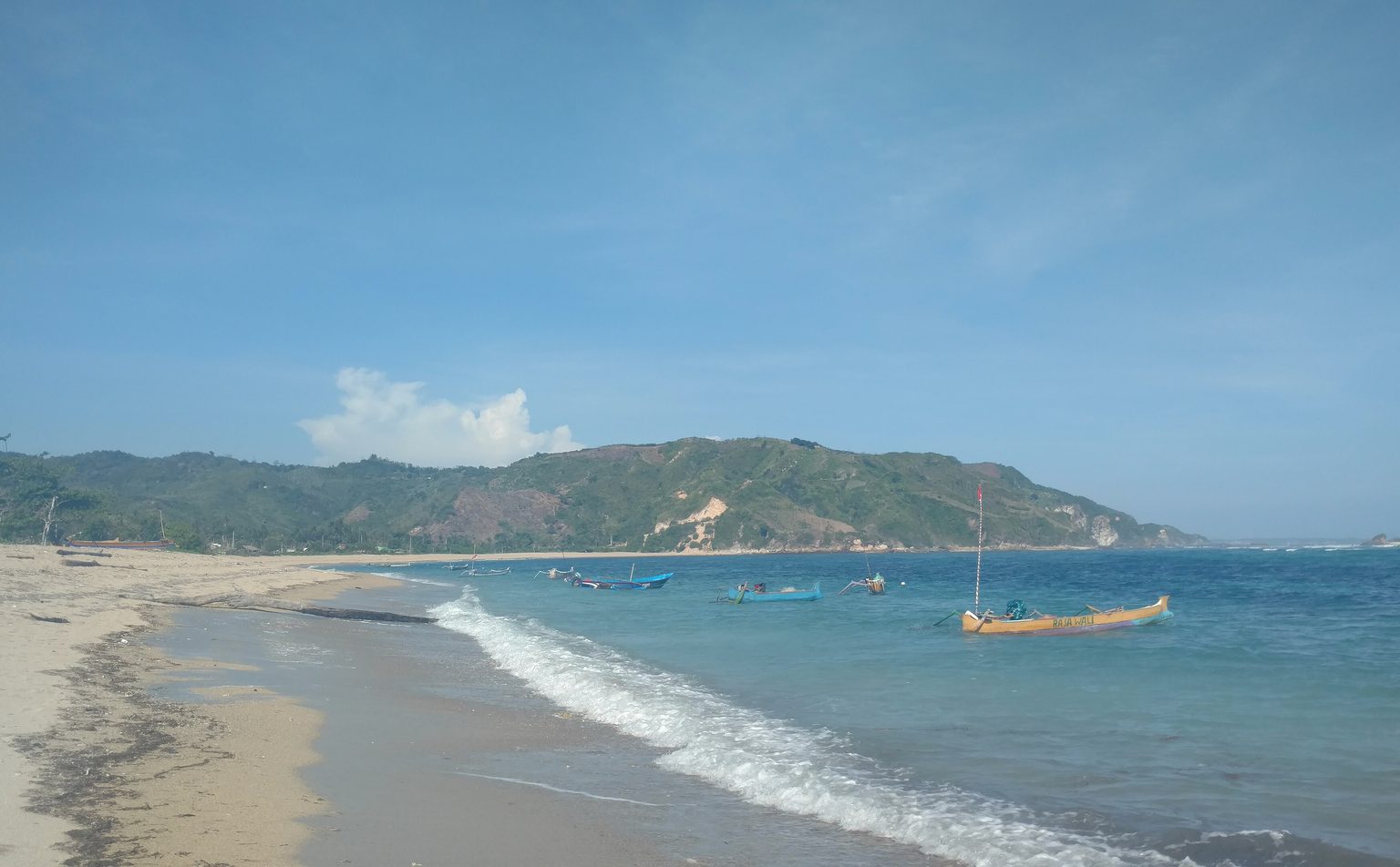 A quiet beach on Lombok with a fishing boat and green hills behind the bay