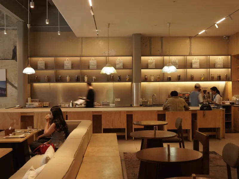 Warm-lit dining room at Tapal Market on Jalan Banceuy, Bandung, with a long wooden counter and café tables