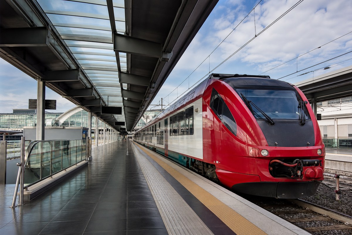 Fiumicino airport rail signs beside a waiting transfer car, suggesting Leonardo Express versus private ride choices