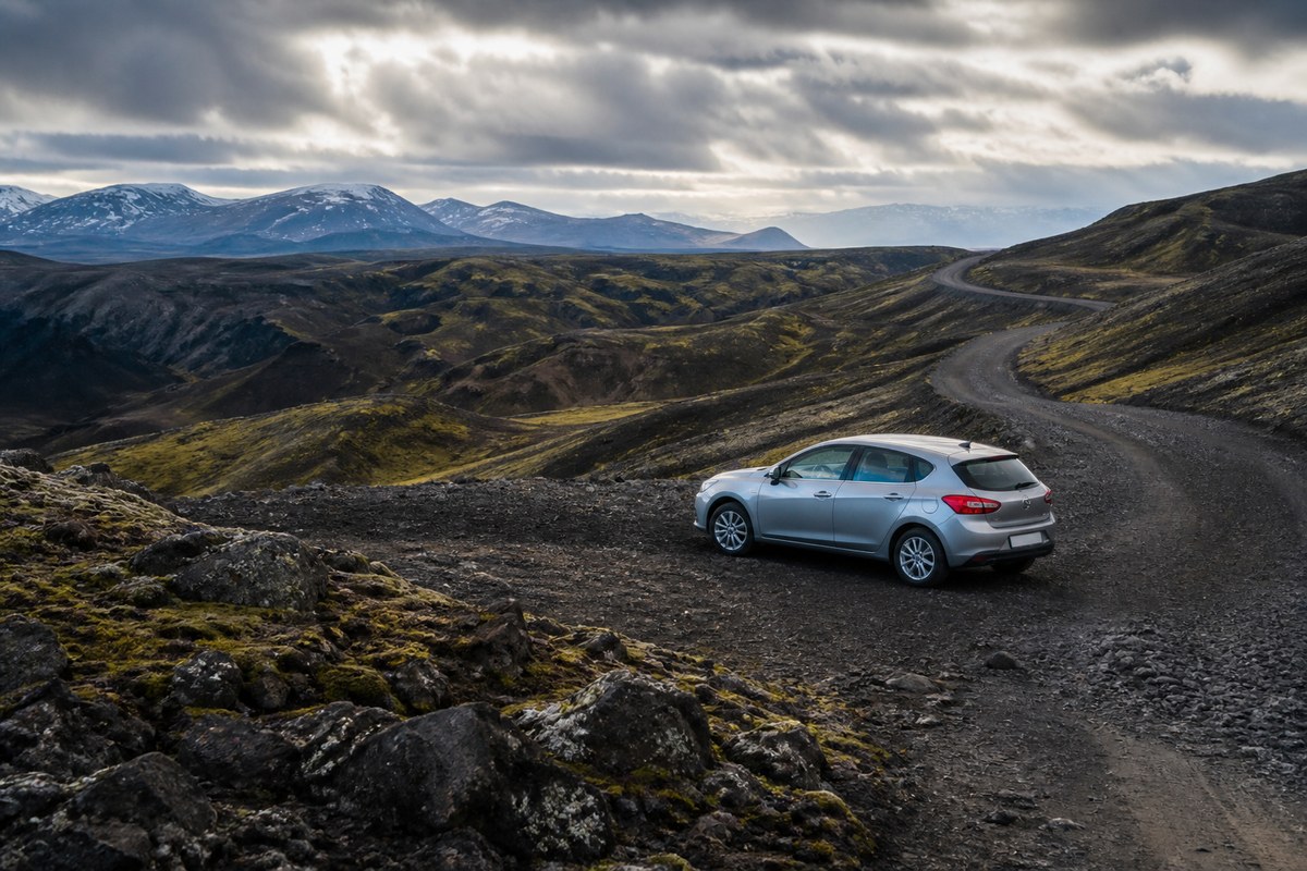 Iceland hire car on a gravel road with distant mountains and low cloud, suggesting F-road and wind-risk planning